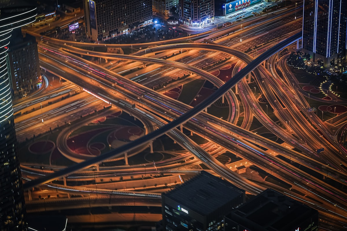 The Sheikh Zayed Road interchange at night, seen from above — a glowing network of mobility infrastructure